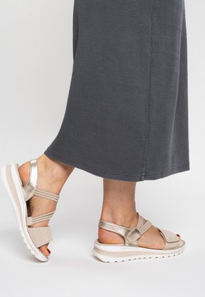 Riemchensandalen in metallischem Gold und Beige mit einer gepolsterten weißen Sohle. Verfügt über mehrere Riemen für sicheren Halt und eine strukturierte Oberseite.