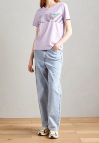Lavendel crew neck t-shirt med sorte horisontale striber og blå grafik, parret med høj talje lyseblå jeans og hvide sneakers.