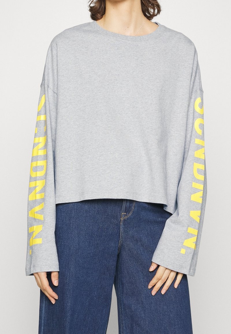 Gray cropped long-sleeve shirt made of cotton, featuring yellow text along the sleeves. The design includes wide sleeves and a casual fit.