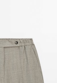 Pantalon gris léger avec une taille élastique et un détail bouton ; doté de plis et d'un tissu texturé.