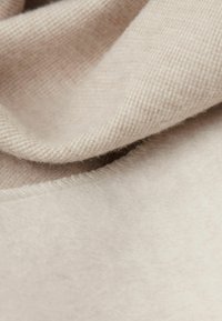 Beżowa tkanina z wełny z domieszką, o miękkiej, teksturowanej powierzchni. Charakteryzuje się gładkim, opadającym krojem oraz delikatnym połyskiem i elastycznymi fałdami.