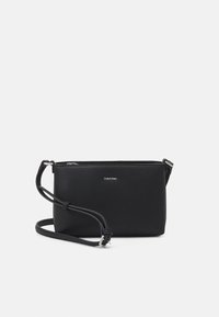 Černá kožená crossbody taška se zipovým uzávěrem, plochým obdélníkovým tvarem, nastavitelným popruhem a stříbrným logem na přední straně.