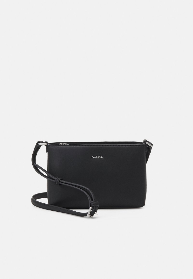 Černá kožená crossbody taška se zipovým uzávěrem, plochým obdélníkovým tvarem, nastavitelným popruhem a stříbrným logem na přední straně.