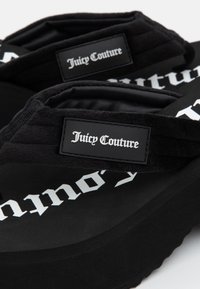 Black flip-flops with velvety straps, featuring a raised black label with "Juicy Couture" in white serif font and a textured sole.