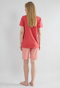 Rode katoenen t-shirt met korte mouwen, gecombineerd met knielange geruite shorts in rood en wit. Eenvoudig ontwerp zonder zichtbare logo's.
