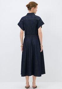 Denim-mekko lyhyillä hihoilla, vyöllä varustettu vyötärö ja A-linjainen hame. Sisältää kultaisia ompeleita ja kaulustakin. Tumma sininen väri.