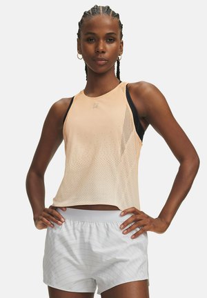 Woman with braided hair wearing a peach sleeveless sports top over a black sports bra and white striped athletic shorts, hands on hips.