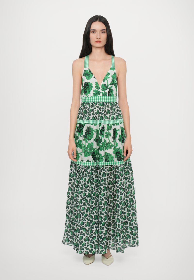 Maxi-jurk met een diepe V-halslijn, groene bladeren en bloemenpatronen, gelaagde stof en gestreepte accenten bij de taille. Gestyled met puntige schoenen.
