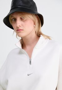 White zip-up sweatshirt with silver Nike logo, paired with a black leather bucket hat. Smooth texture with a high collar and shiny zipper.