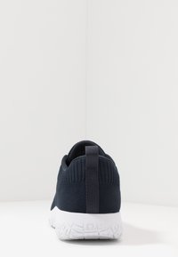 Tmavě modrá sportovní obuv s prodyšným svrškem, polstrovaným límcem a kontrastní bílou gumovou podešví, která obsahuje zadní poutko pro snadné obouvání.