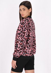 Giacca bomber in stampa leopardo rosa e nera con polsini e orlo a coste, dal finish satinate, indossata sopra pantaloni corti neri.