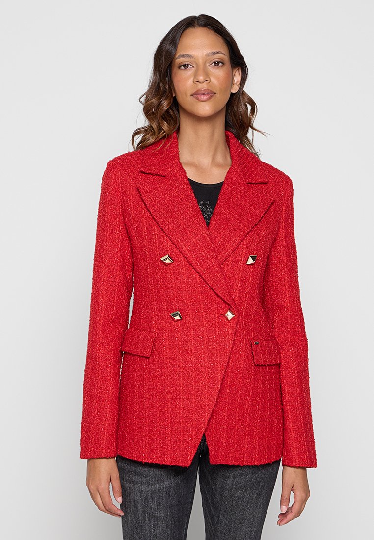 Giacca rossa doppiopetto realizzata in tessuto strutturato, con borchie a piramide dorate, revers con alette e due tasche frontali.