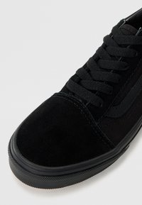 Baskets noires avec une tige en daim et textile, six œillets avec des lacets noirs plats, semelle extérieure en caoutchouc et accents latéraux texturés.