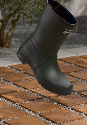 Green rubber boot with a plaid interior design, rounded shape, textured sole for grip, displayed above a patterned tile surface.