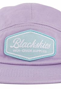 Violeta cepure ar teksturētu audumu, kas rotāta ar gaiši zilo sešstūra plāksteri ar balti izšūtu tekstu "Blackskies" un "HIGH-GRADE SUPPLIES."
