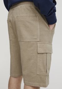 Bermudas cargo beige fabricadas en una suave mezcla de algodón, con múltiples bolsillos, costuras decorativas y una cintura elástica. Parche del logo en la parte trasera.