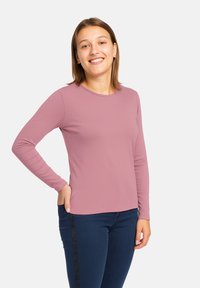 Top aderente con maniche lunghe in un delicato color malva, realizzato in un tessuto liscio ed elastico. Indossato con jeans blu scuro dotati di una striscia di accento laterale.