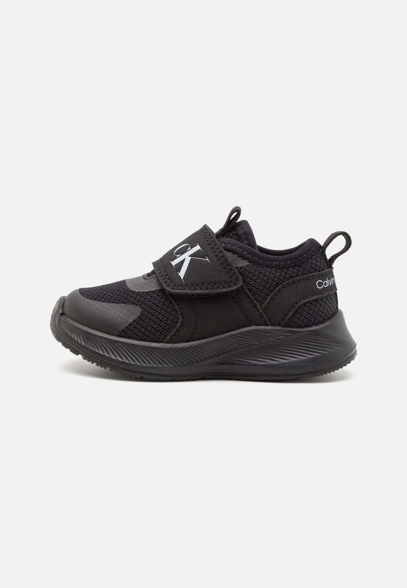 Black athletic shoes with a mix of mesh and synthetic materials. Features a hook-and-loop strap and textured rubber sole for grip.