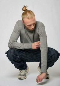 Un pull en tricot gris avec des détails côtelés sur les épaules, associé à un pantalon cargo à motifs navy. Des baskets blanches et grises.