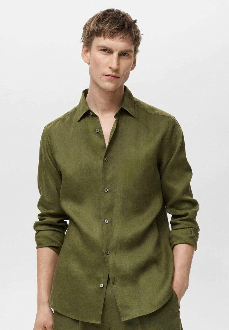 Camicia verde oliva con bottoni, maniche lunghe e colletto appuntito, realizzata in un tessuto testurizzato, con bottoni frontali e polsini arrotolati.