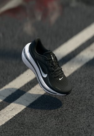 Schwarz-weißer Nike-Laufschuh in der Luft über einer Asphaltstraße mit weißen Fahrbahnmarkierungen.