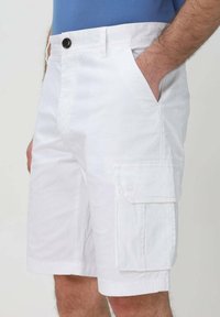 Bermuda bianche realizzate in cotone, dotate di tasche laterali e chiusura frontale con bottone. Il tessuto ha una consistenza liscia ed è di lunghezza al ginocchio.