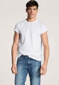 Weißes Baumwoll-T-Shirt mit kurzen, umgeschlagenen Ärmeln, Rundhalsausschnitt und lässiger Passform, kombiniert mit blauen Jeans aus Denim mit einem ausgewaschenen Look.