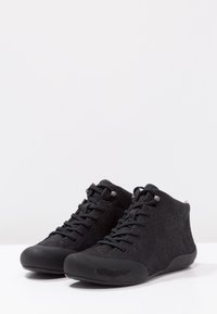Black high-top shoes with textured fabric upper, rubber soles, and shiny accents. Features tonal laces and a minimalistic design.