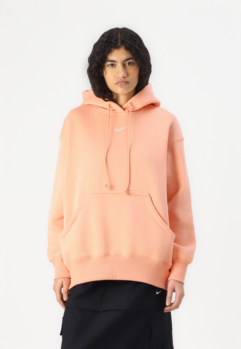 Sweat-shirt à capuche en rose pastel, fabriqué en tissu doux. Il dispose d'une poche avant, de poignets côtelés et d'un logo discret sur la poitrine.