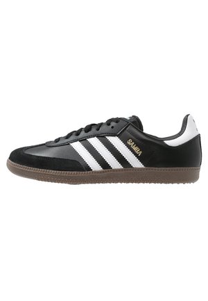 Czarny sneaker Adidas Samba z białymi paskami, gumową podeszwą i napisem "SAMBA" w złotych literach po boku.