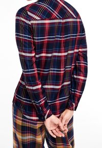 Röd, marinblå och gul rutig långärmad skjorta med rak klippning bak, knappade manschetter och yoke-design. Materialet verkar lätt och vävt.