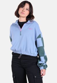 Pull en polaire bleu clair avec fermeture éclair à mi-hauteur, manches à carreaux verts, Ourlet élastique et détails de fermeture éclair roses.
