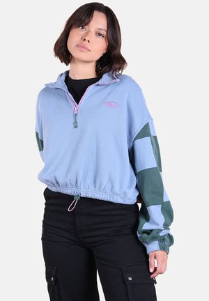Pull en polaire bleu clair avec fermeture éclair à mi-hauteur, manches à carreaux verts, Ourlet élastique et détails de fermeture éclair roses.