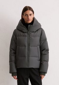 Donkergrijze pufferjack met een brede, opvouwbare capuchon, een ritssluiting aan de voorkant en grote, gepleisterde delen. Geribbelde manchetten zorgen voor extra warmte en textuur.