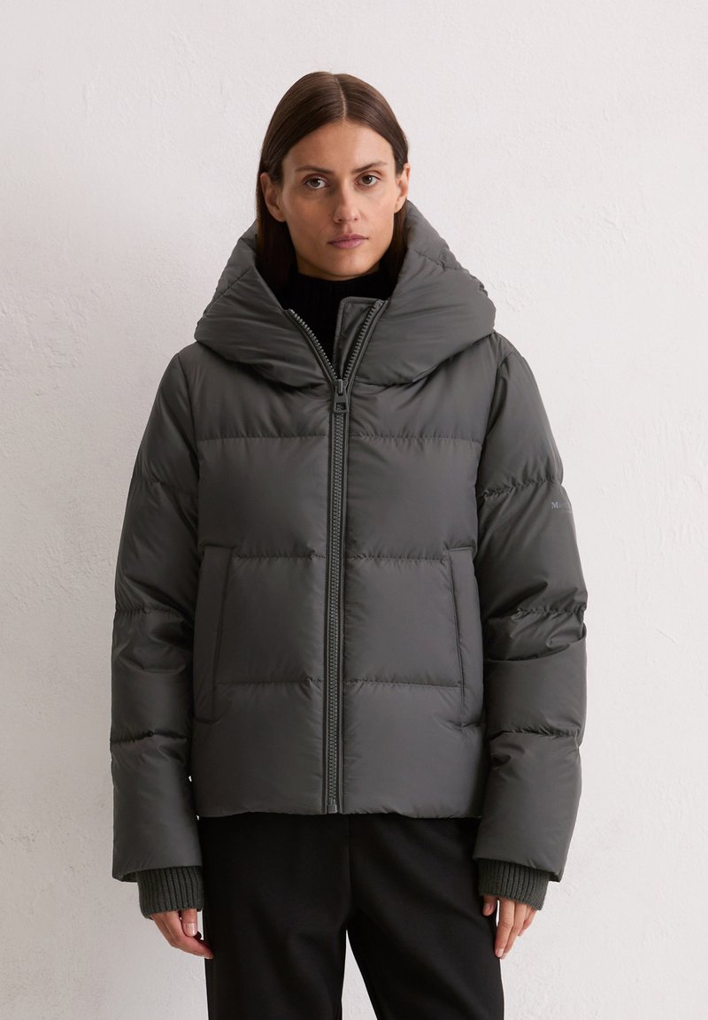 Donkergrijze pufferjack met een brede, opvouwbare capuchon, een ritssluiting aan de voorkant en grote, gepleisterde delen. Geribbelde manchetten zorgen voor extra warmte en textuur.