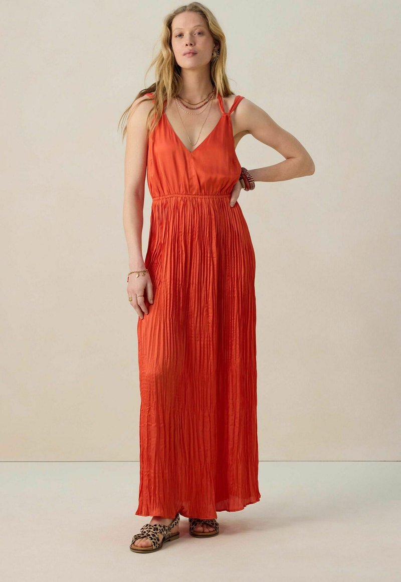 Robe longue sans manches en V de couleur orange vif avec une texture plissée, taille cintrée, portée avec des sandales à imprimé animal.