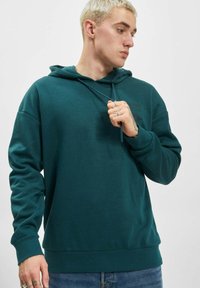 Teal hettegenser laget av mykt stoff, med kengurulomme, justerbare snorer og ribbede mansjetter.