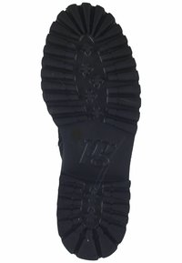 Suela de zapato de goma negra con profundos surcos y ranuras, con un logotipo centrado. La superficie muestra detalles texturales y patrones para una mejor tracción.