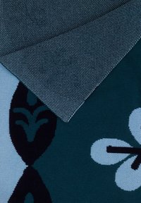 Tkanina z ciemnozielonym tłem i wzorem kwiatowym w jasnoniebieskich oraz czarnych akcentach. W jednym rogu widoczna jest szara tekstura geometryczna.