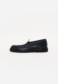 Navy leather shoe with a textured finish, featuring a large white flap on the toe and a low black sole. Classic, minimalist design.