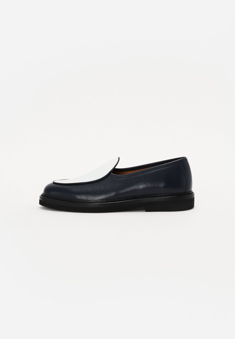 Navy leather shoe with a textured finish, featuring a large white flap on the toe and a low black sole. Classic, minimalist design.