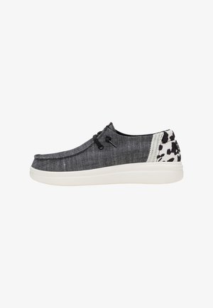 Scarpa da barca in denim nero con suola bianca, dotata di lacci neri e un motivo decorativo sul tallone. Texture liscia con design informale.
