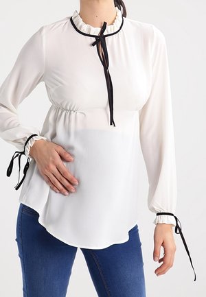 Blusa blanca de manga larga con cuello fruncido, detalle de lazo negro y puños elásticos. Tejido suave y ligero con un ajuste fluido.