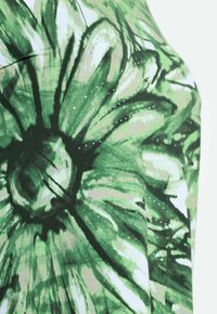 Zielona tkanina w kwiatowy wzór z dużymi nadrukami stokrotek, ozdobiona błyszczącymi akcentami i miękką fakturą. Głównie zielone odcienie z białymi detalami.