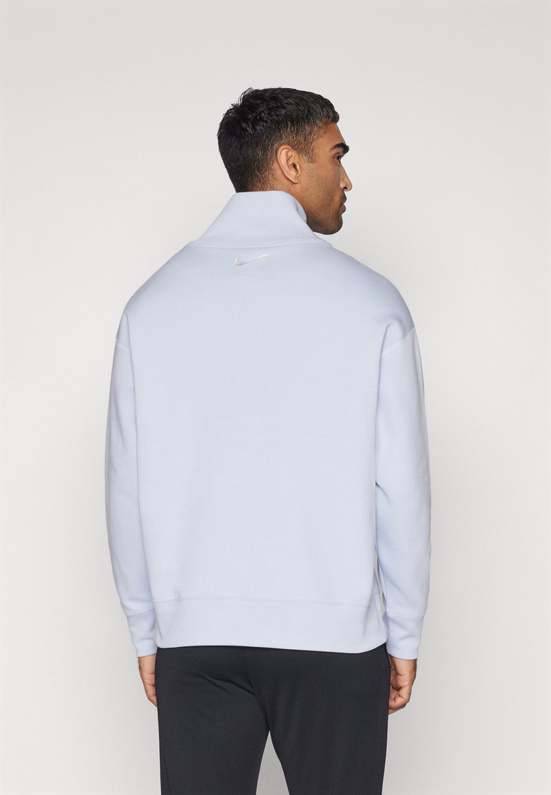 Felpa leggera di colore blu chiaro con colletto alto, caratterizzata da un sottile logo Nike sul retro. Texture morbida e polsini a coste. Design semplice.