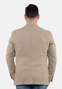 Blazer beige strutturato con una vestibilità su misura, spacco singolo sul retro e maniche lunghe. Presenta una chiusura a due bottoni e un motivo sottile.