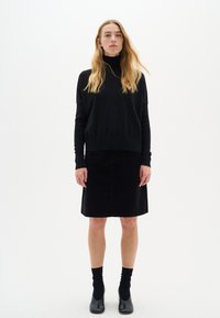 Czarny sweter w golf i czarna spódnica z korduroju, obie z luźnym fasonem. Nosi się z czarnymi skarpetkami do kostek i czarnymi butami. Minimalistyczny design.