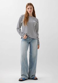 Striped long-sleeve top in white and navy, paired with light blue wide-leg jeans. Footwear features blue and black sandals with accents.