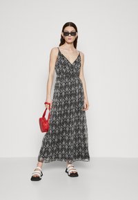 Rochie maxi cu model alb și negru, cu decolteu în V și bretele subțiri, din țesătură texturată, asortată cu o poșetă roșie și sandale albe.
