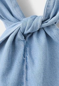 Tissu en denim bleu clair noué en un simple nœud, montrant la texture et les détails des coutures sur un fond uni.
